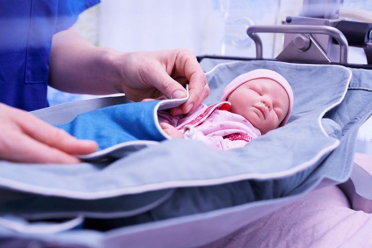 Krankenschwester umsorgt Frühgeborenenpuppe in einer Hängematte im Inkubator